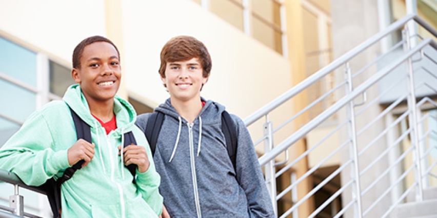Two young men with backpacks stand next to each other smiling